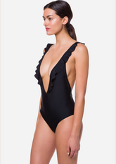 Model wearing The Plunge One Piece Swimsuit with deep V neckline, ruffle detail, and adjustable straps — designer swimwear made for bold beach moments